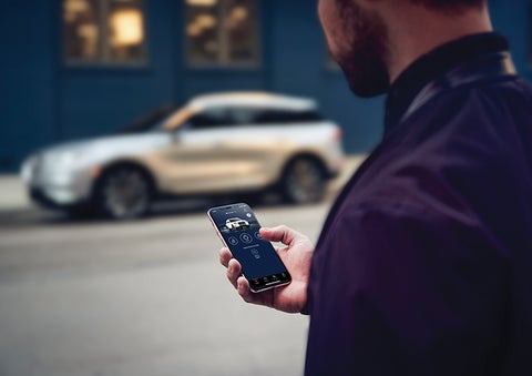 A person is shown interacting with a smartphone to connect to a Lincoln vehicle across the street. | Buss Lincoln in McHenry IL
