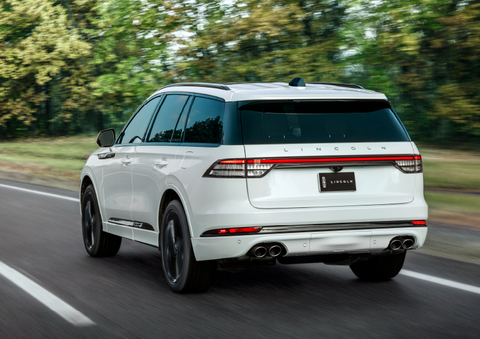 A white 2025 Lincoln Aviator® SUV is being driven away down a road lined with colorful trees. | Buss Lincoln in McHenry IL