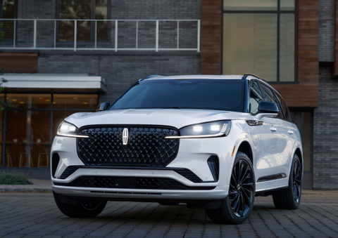 A white 2025 Lincoln Aviator® SUV is shown parked outside a modern building with gray brick and wood accents. | Buss Lincoln in McHenry IL