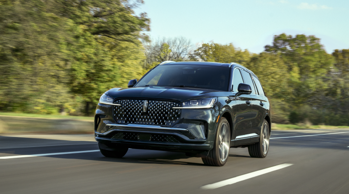 A 2025 Lincoln Black Label Aviator® SUV is being driven down a road lined with trees. | Buss Lincoln in McHenry IL