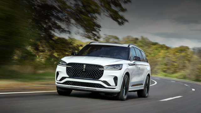 A white 2025 Lincoln Aviator® SUV is being driven down a road lined with trees. | Buss Lincoln in McHenry IL