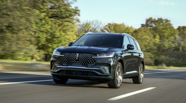 A 2026 Lincoln Black Label™ Aviator® SUV is being driven down a road lined with trees. | Buss Lincoln in McHenry IL