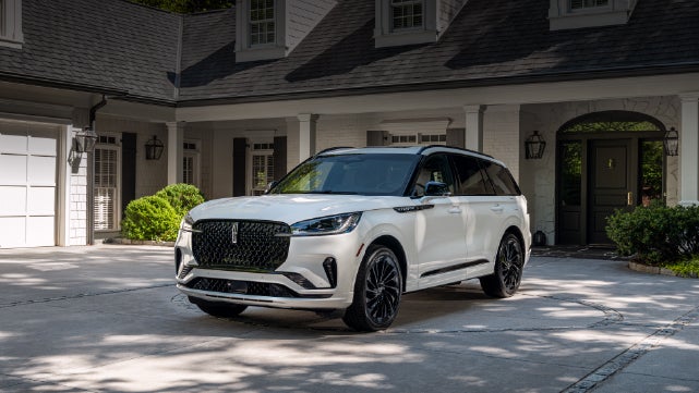 A white 2026 Lincoln Aviator® SUV is parked in the driveway of a luxury home. | Buss Lincoln in McHenry IL