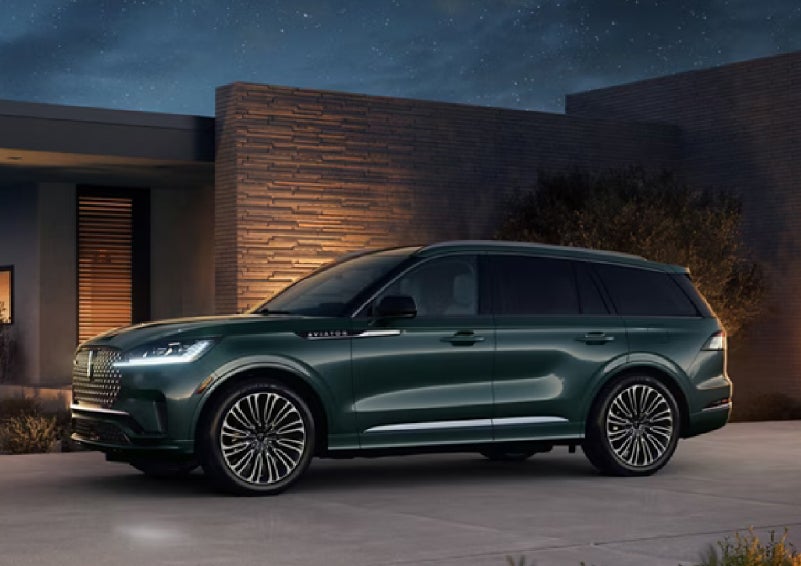 A green 2027 Lincoln Aviator® SUV is parked outside a contemporary home. | Buss Lincoln in McHenry IL