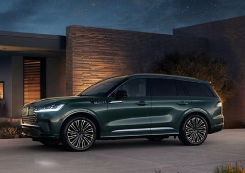 A green 2027 Lincoln Aviator® SUV is parked outside a contemporary home. | Buss Lincoln in McHenry IL