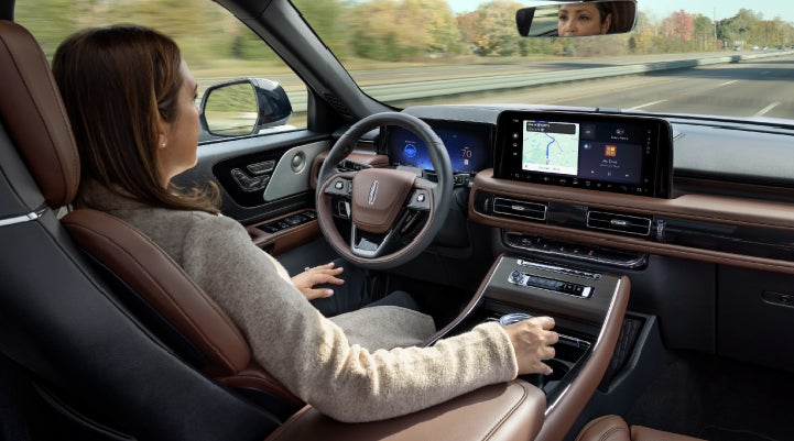 A 2027 Lincoln Aviator® SUV is being driven hands-free on a highway lined with trees. | Buss Lincoln in McHenry IL