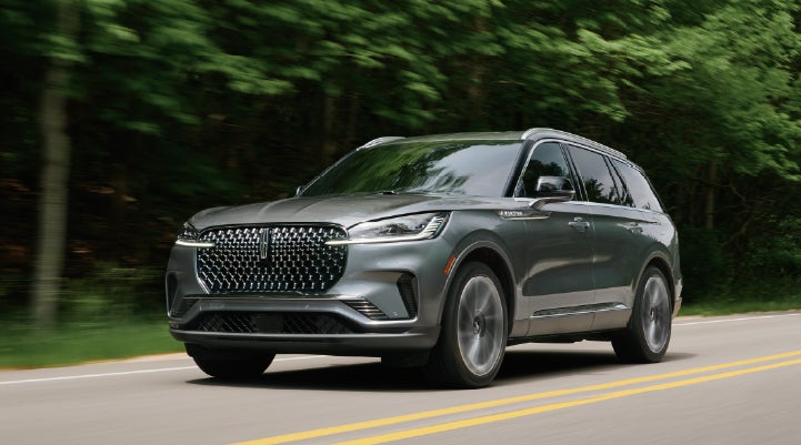 A 2027 Lincoln Aviator® SUV is being driven down a road lined with trees. | Buss Lincoln in McHenry IL
